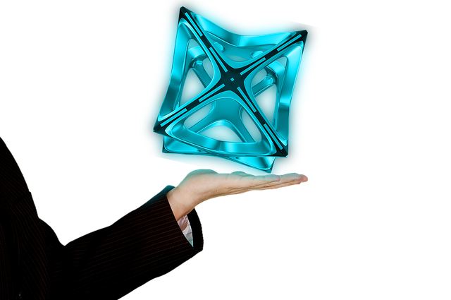 Outstretched hand in a dark suit sleeve presents a blue, glassy, X-shaped geometric sculpture floating above the palm