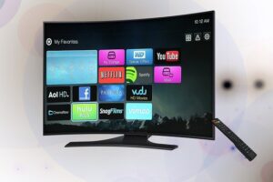 Curved flat-screen smart TV on a stand showing colorful streaming app icons; a black remote rests to the right.