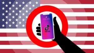 Silhouette hand holding a smartphone showing the TikTok logo inside a red prohibition circle, with a US flag backdrop.