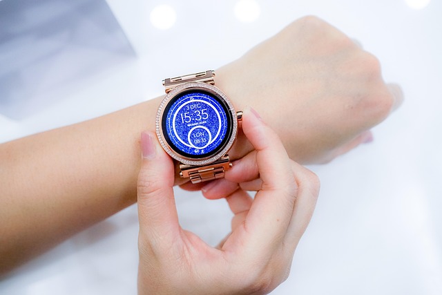 Rose-gold smartwatch on a wrist being fastened by hands, blue digital display visible in the watch face.