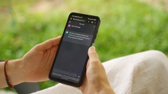 Person holds a smartphone outdoors; the screen shows a notification banner in dark mode.
