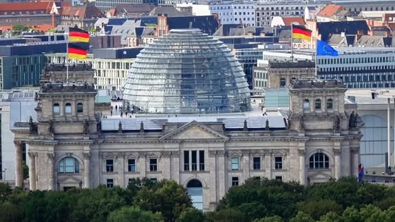 Berlin's Reichstag building with its glass dome and flags atop, set against a city skyline.