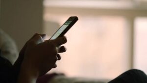 Hands holding a smartphone, screen glowing in a dim room.