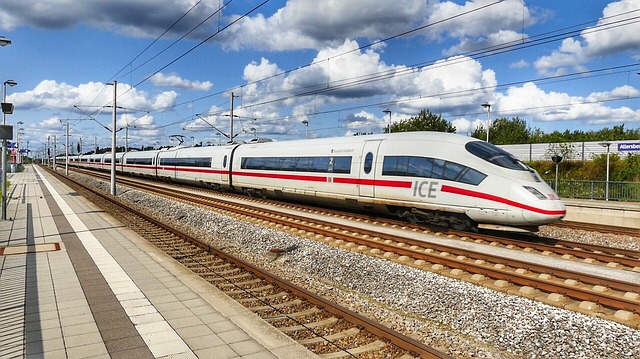 High-speed ICE train on a platform with blue sky and clouds, white body with red stripe, multiple cars extending into the distance