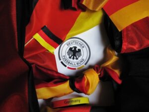Close-up of a German flag-colored scarf with a circular Deutscher Fußball-Bund (DFB) logo amid red, black, and gold fabric pieces; a yellow wristband labeled 'Germany' is also visible.