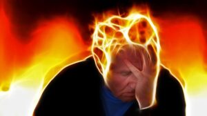 A man sitting with his head in his hand, surrounded by intense orange-yellow flames, signaling extreme heat or stress.
