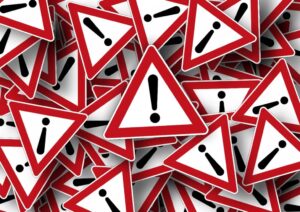 Pile of red triangular warning signs with black exclamation marks, overlapping across the image.