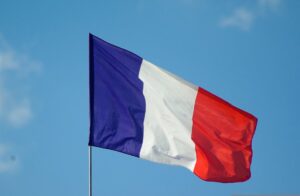 French flag waving on a flagpole against a blue sky with light clouds